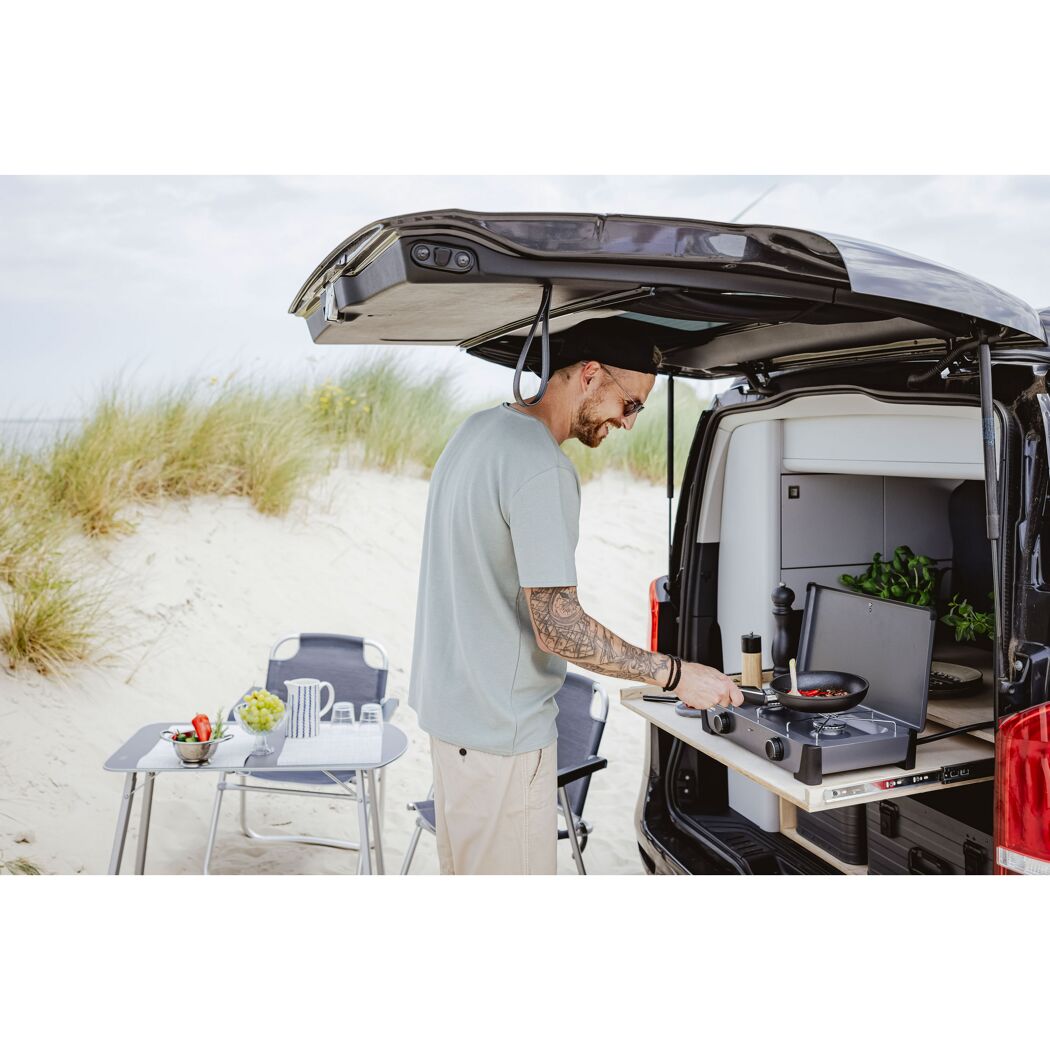 Person kocht auf Campingkocher am Strand