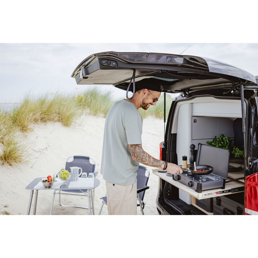 Person kocht auf Campingkocher am Strand