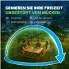 Lachende Personen mit Mückenabwehrgerät an Tisch im Grünen.