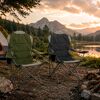 Zwei Campingstühle am Seeufer vor Bergkulisse.
