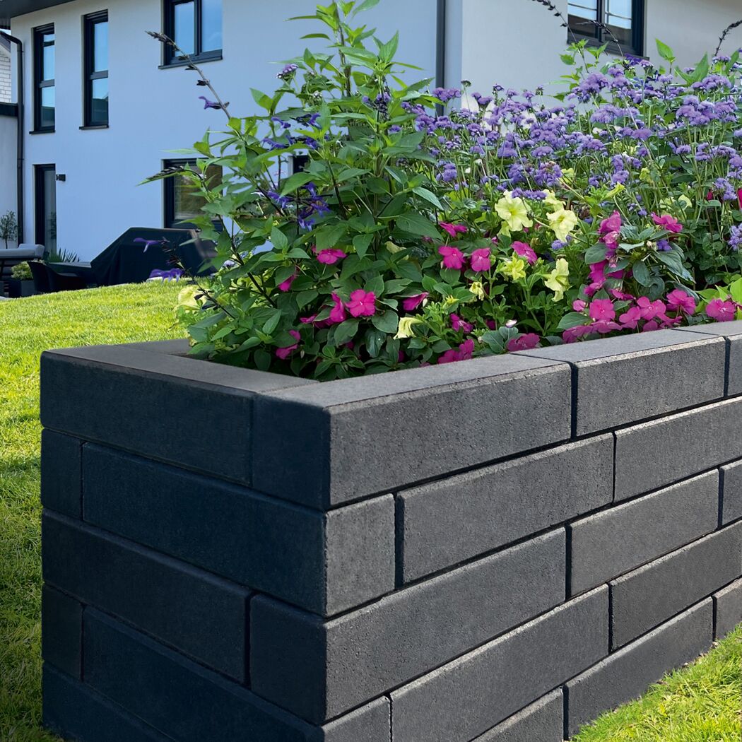 Basaltfarbener Mauerstein 'T-Wall Fine' als Hochbeet mit Blumen.
