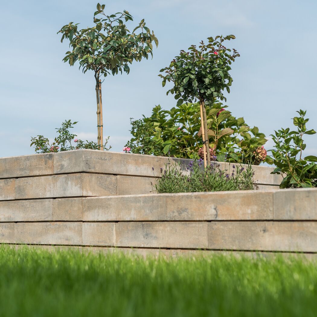 Mauerstein 'T-Wall Linear' als Gartenmauer mit Pflanzen und Gras.