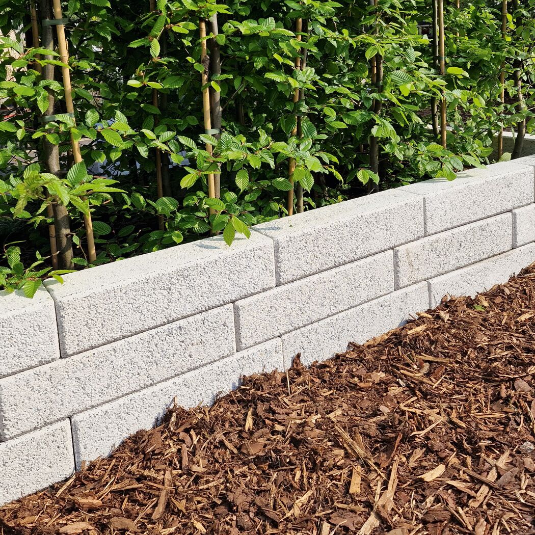 Granitfarbene Mauersteine mit grüner Hecke und Rindenmulch im Garten.