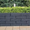 Basaltfarbener Mauerstein 'T-Wall Castra' vor Hecke.