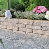 Mauerstein 'T-Wall Castra' als Gartenmauer mit Blumen und Frosch.