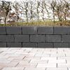 Mauer aus basaltfarbenen Mauersteinen mit heller Pflasterung im Vordergrund.