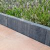 Graphitfarbene Palisade grenzt Blumenbeet und Terrassenplatten ab.