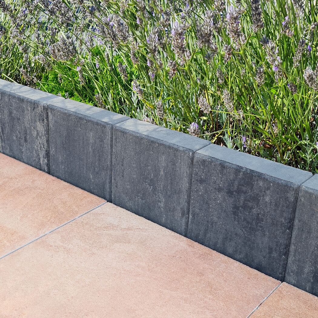 Graphitfarbene Palisade grenzt Blumenbeet und Terrassenplatten ab.