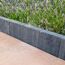 Graphitfarbene Palisade grenzt Blumenbeet und Terrassenplatten ab.