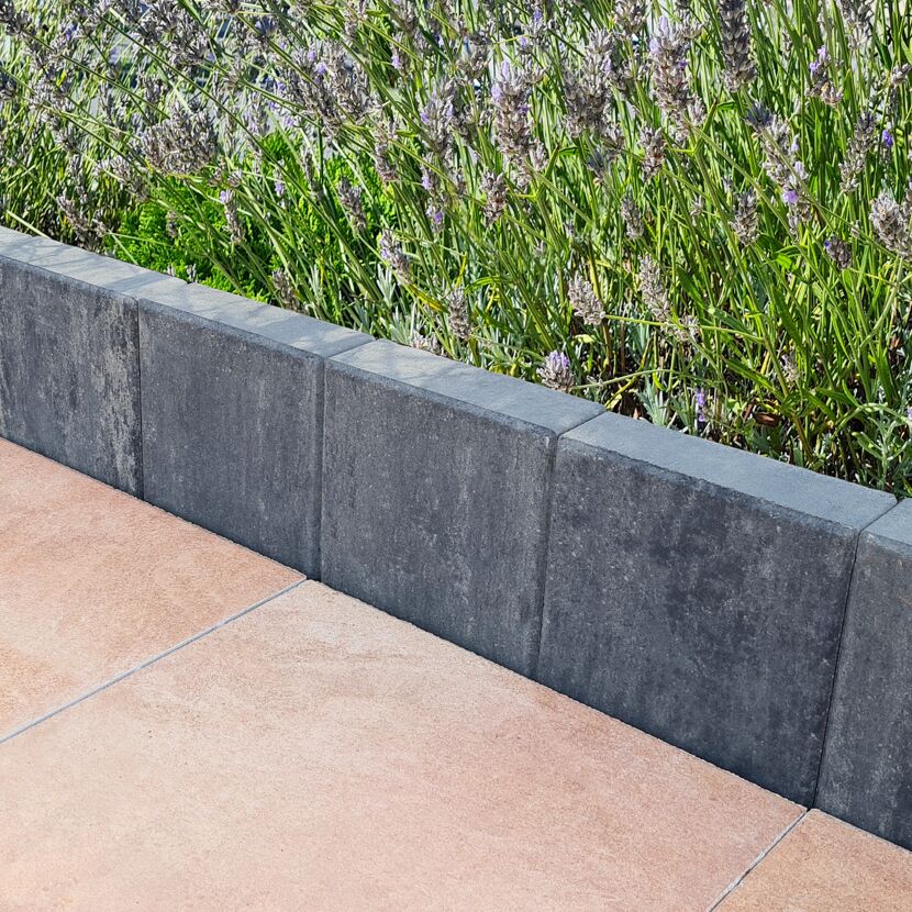 Graphitfarbene Palisade grenzt Blumenbeet und Terrassenplatten ab.