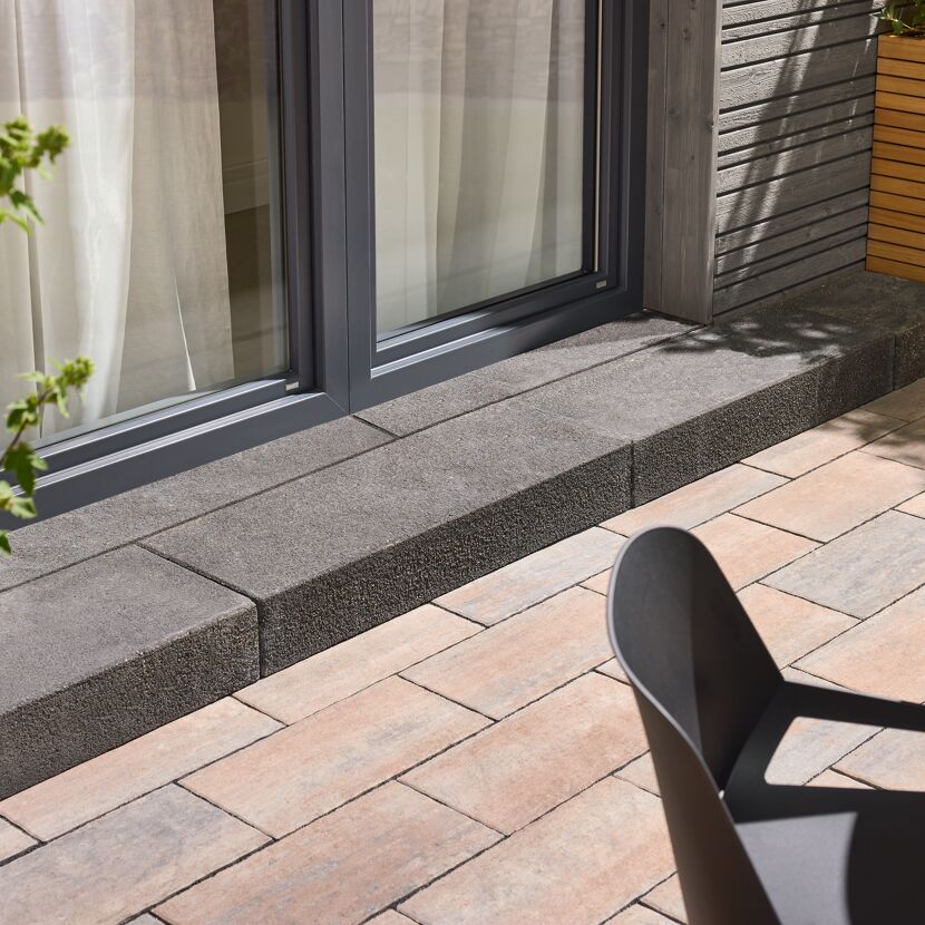 Basaltfarbene Blockstufe 'T-Stair Shine' vor einer Fenstertür.