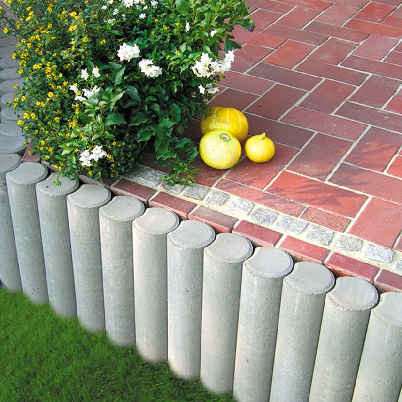 Graue Palisaden grenzen Gartenweg und Grasfläche ab.