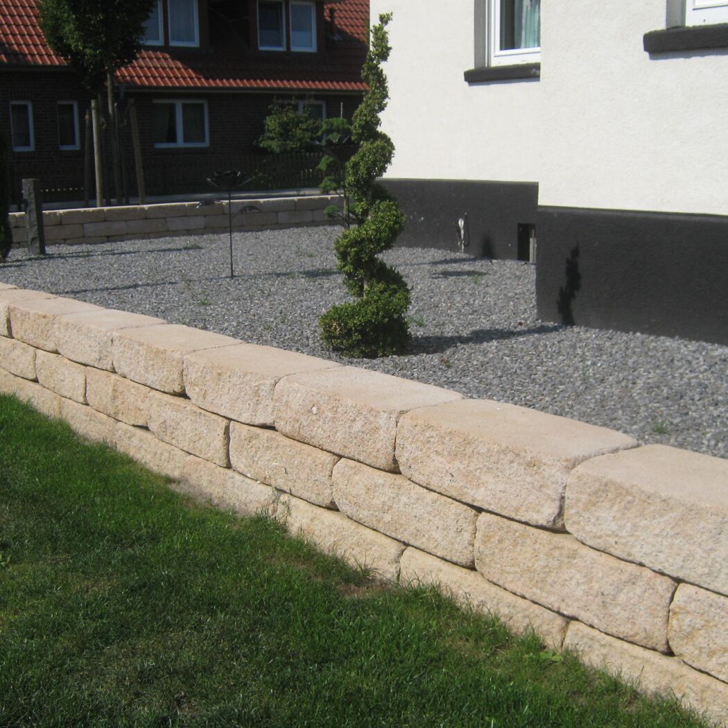 Sandsteinfarbene Mauersteine als Gartenbegrenzung mit Rasen.