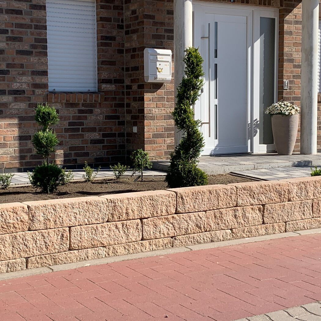 Sandsteinfarbene Mauersteine 'T-Wall Quarry Mini' als Beetbegrenzung vor Haus.