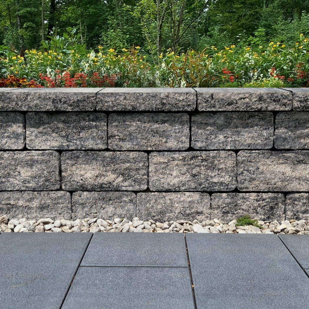 Mauerstein 'T-Wall Quarry Block' im Garten mit Blumenbeet.