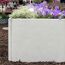 Graue Palisade mit lila und weißen Blumen bepflanzt.