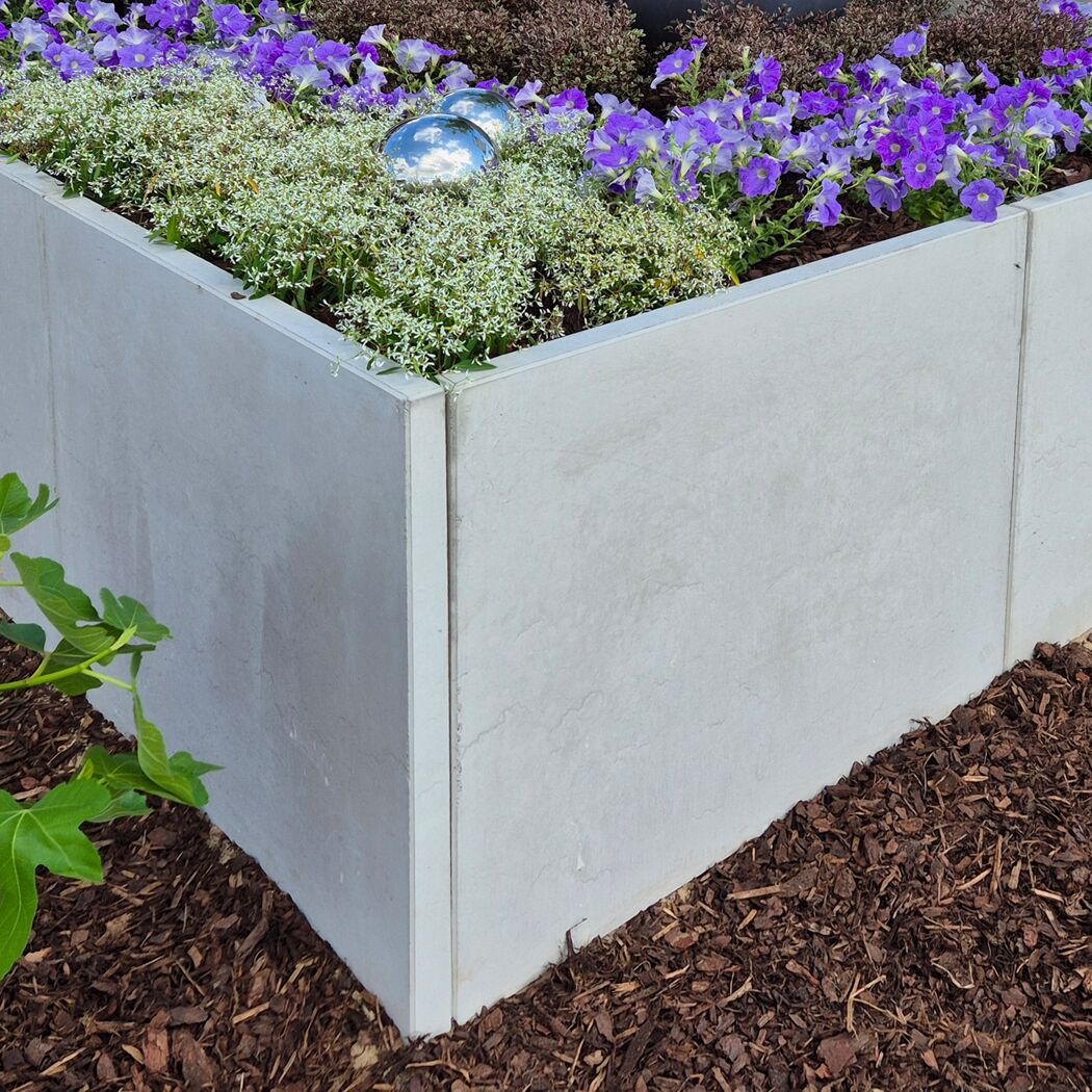 L-Stein-Ecke grau mit Blumen bepflanzt, umgeben von Rindenmulch.