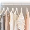 Weiße Formkleiderbügel mit hängender heller Kleidung.