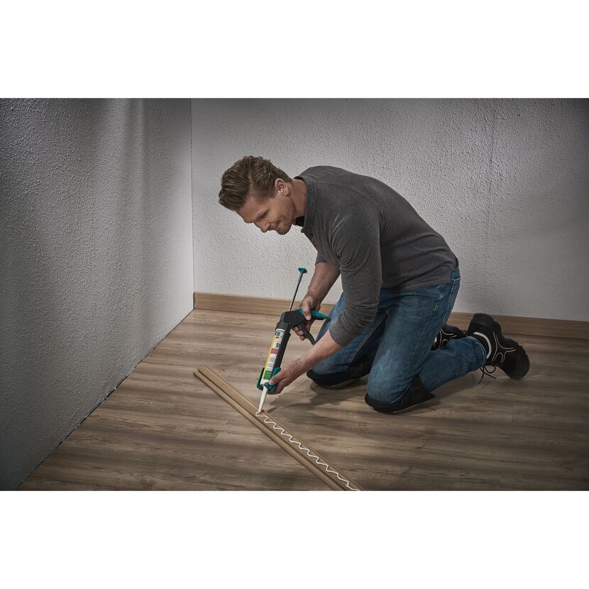 Person verklebt Sockelleisten mit Kartuschenpistole.