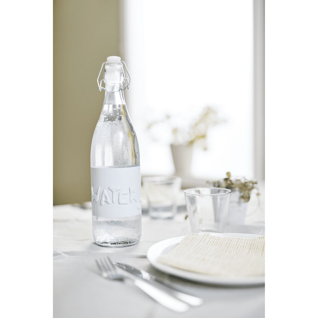Glasflasche mit Wasser und Etikett auf gedecktem Tisch