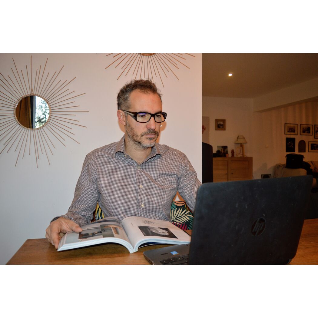 Person liest in einem Magazin und schaut auf einen Laptop.