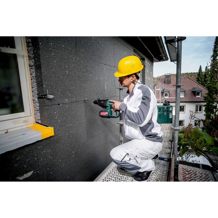 Person verwendet einen Bohrhammer an einer Hauswand.
