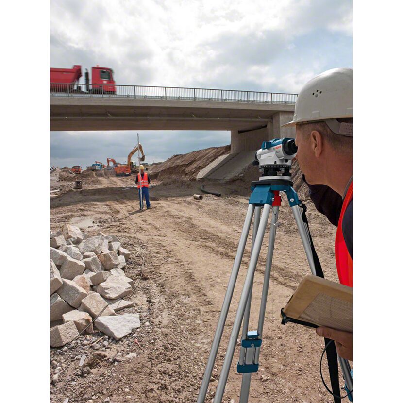 Person mit optischem Nivelliergerät auf Baustelle