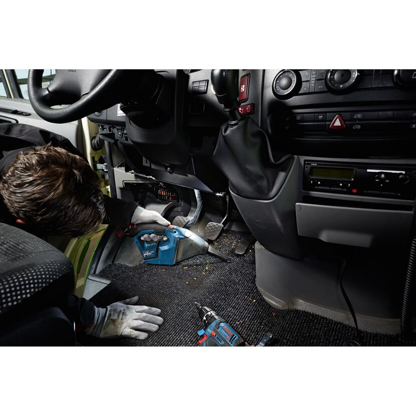 Person saugt Fußraum im Auto aus