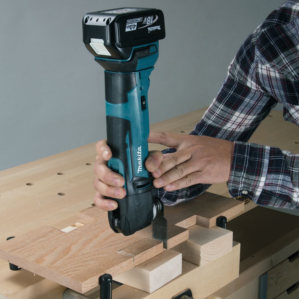 Person sägt mit einem Makita Multifunktionswerkzeug in ein Stück Holz.