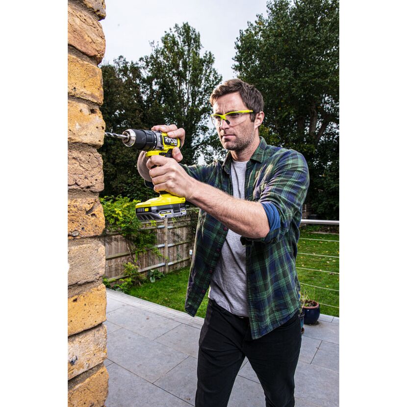 Person bohrt mit einem RYOBI Schlagbohrschrauber in eine Backsteinmauer.
