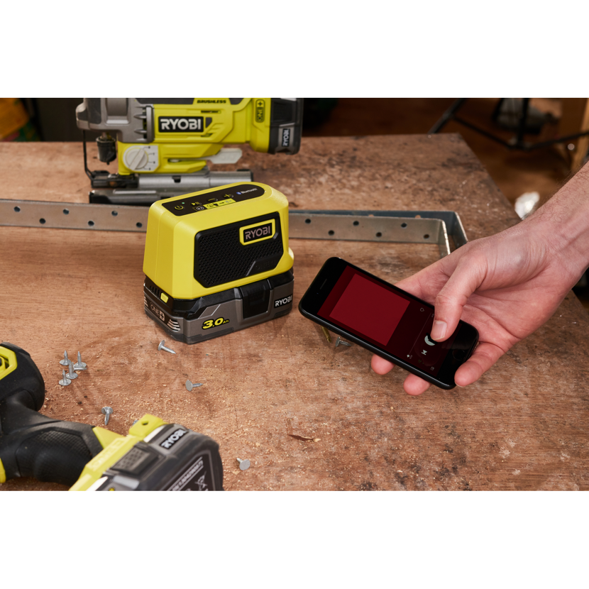 Person steuert Ryobi Bluetooth-Lautsprecher mit Handy