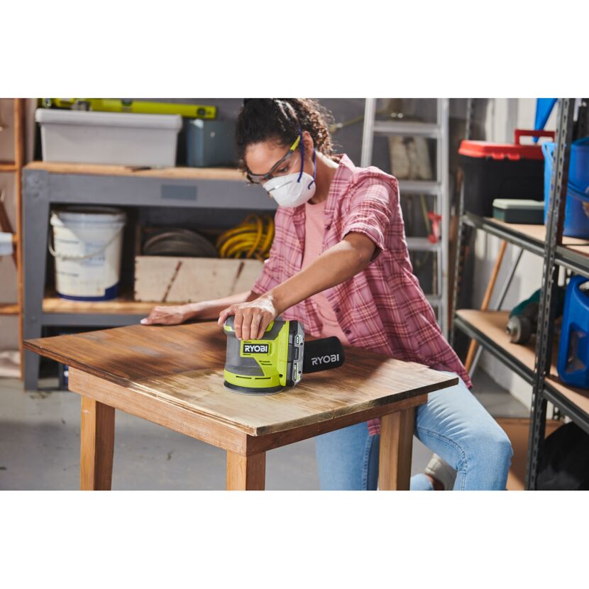Person schleift einen Tisch mit einem RYOBI Exzenterschleifer.