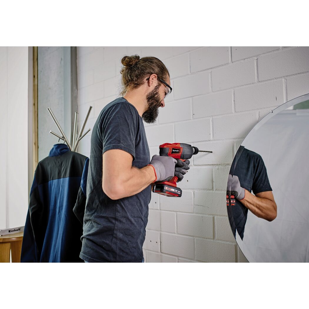 Person bohrt mit einem Akku-Bohrhammer in eine weiße Wand.