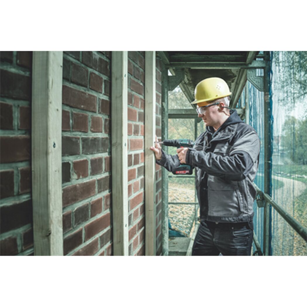 Person bohrt mit einem Akku-Schlagbohrschrauber in eine Backsteinwand.