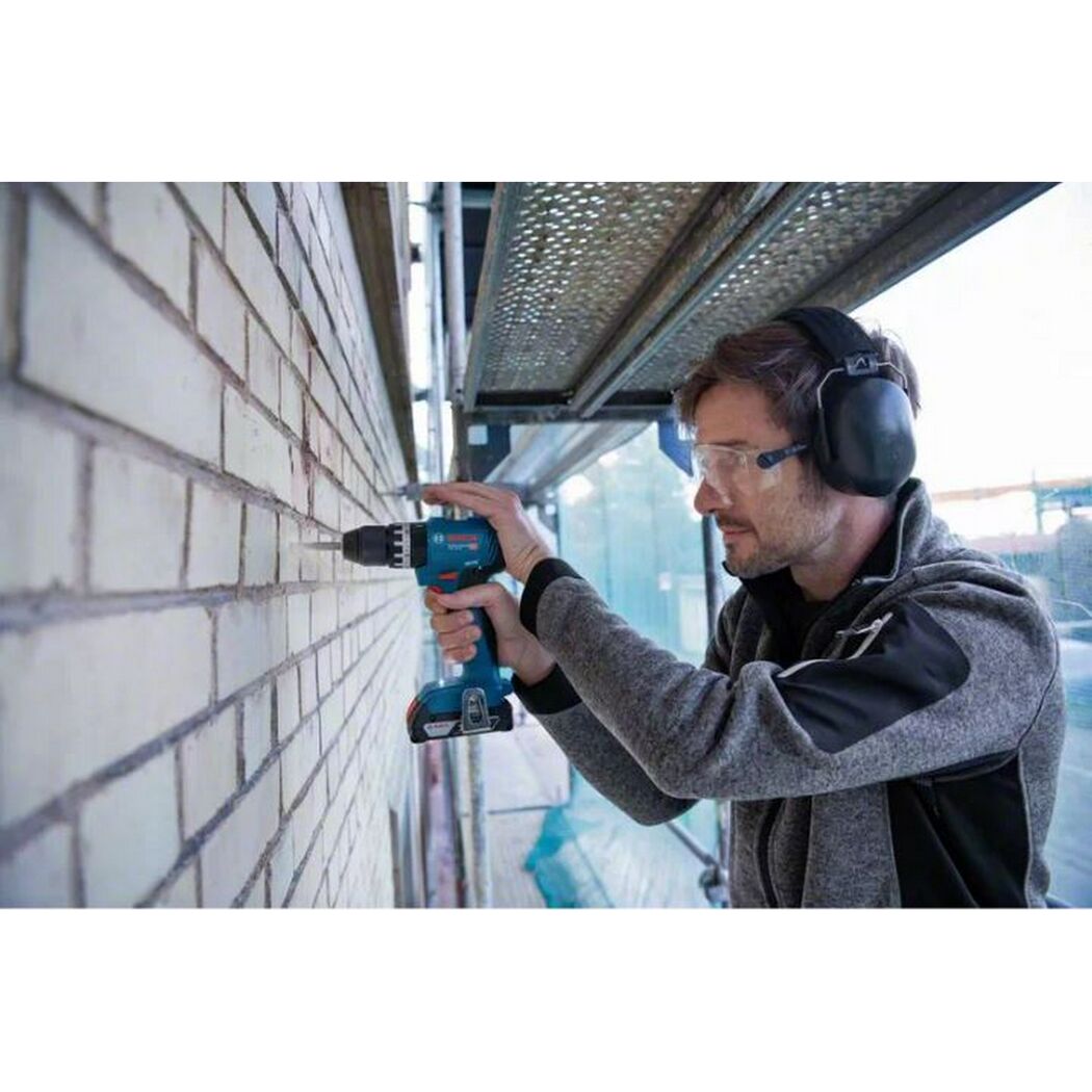 Person bohrt mit Akkubohrschrauber in eine Ziegelwand.