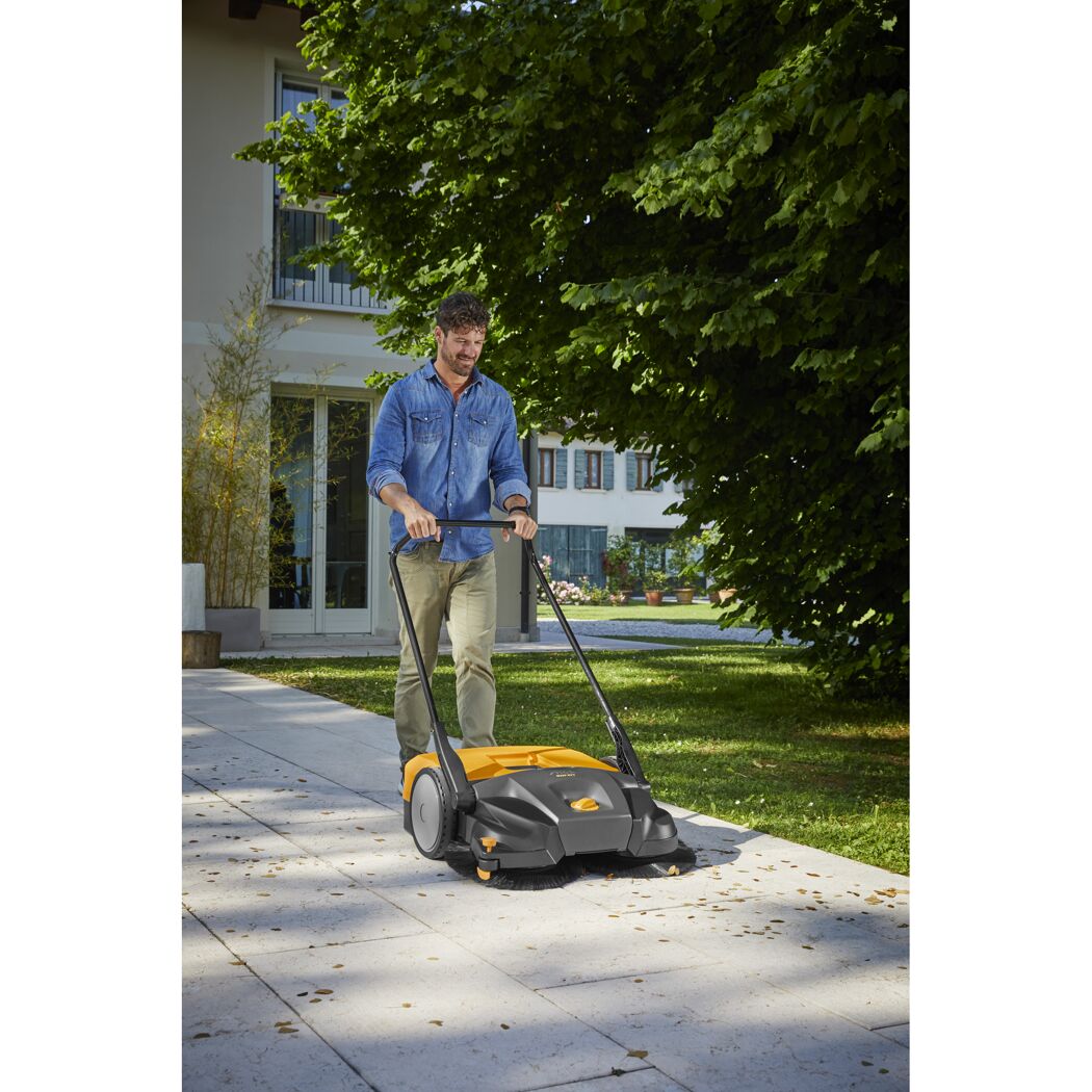 Person kehrt Blätter mit Kehrmaschine.