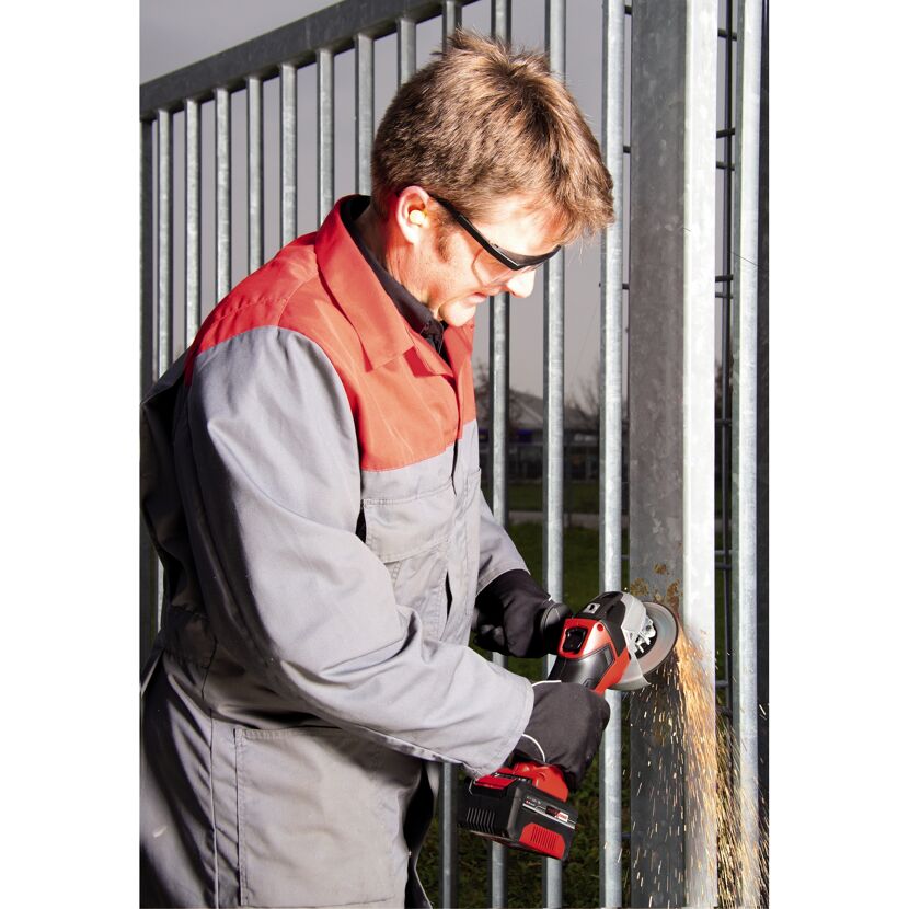 Person schleift mit einem Winkelschleifer ein Metalltor.