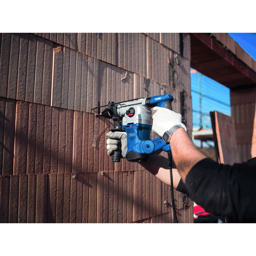 Person bohrt mit einem Bohrhammer in eine Ziegelwand.