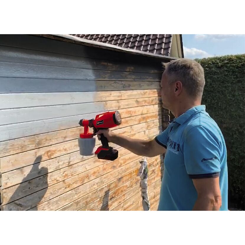 Person streicht Holzfassade mit Farbsprühsystem