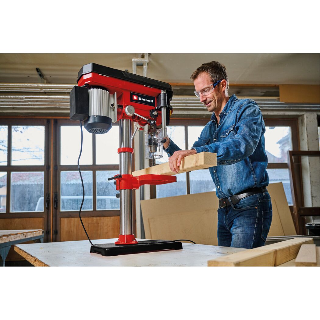 Person bohrt mit einer Säulenbohrmaschine in ein Holzstück.