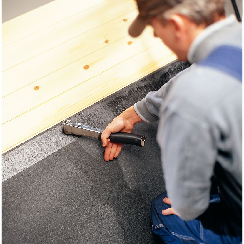 Person befestigt Dachpappe mit Hammertacker