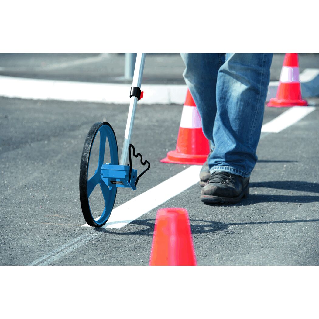 Person misst mit Messrad eine weiße Linie auf Asphalt ab.