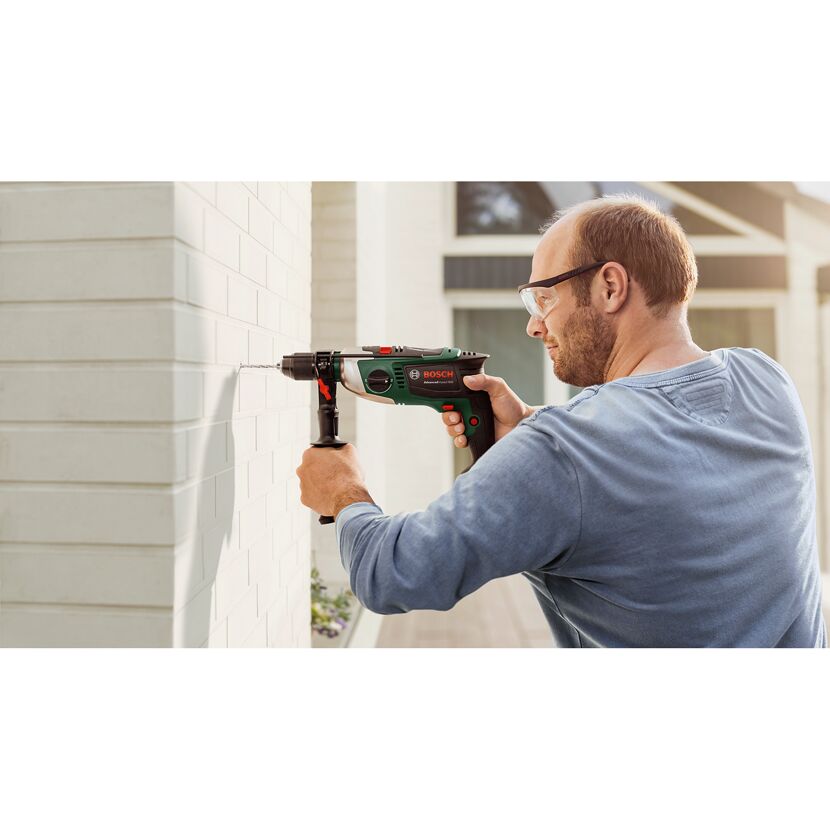 Person bohrt mit der Schlagbohrmaschine AdvancedImpact 900 ein Loch in eine weiße Wand.