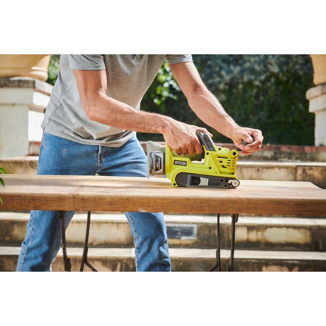 Person schleift Holztisch mit RYOBI Akku-Bandschleifer