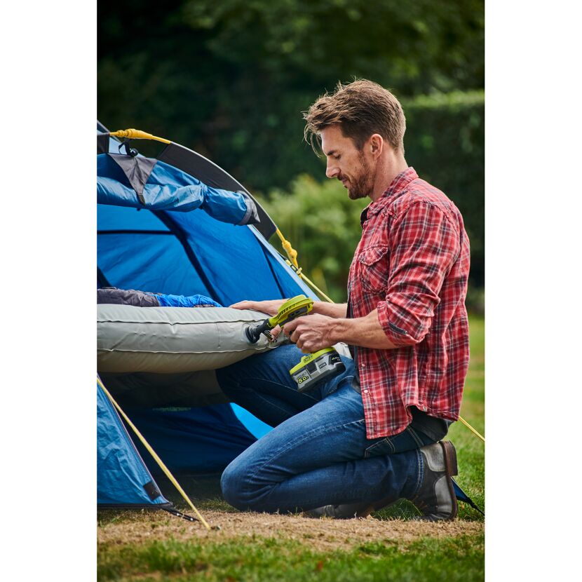 Person pumpt mit RYOBI Akku-Luftpumpe eine Luftmatratze im Zelt auf.