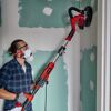 Person schleift mit Trockenbauschleifer eine Wand