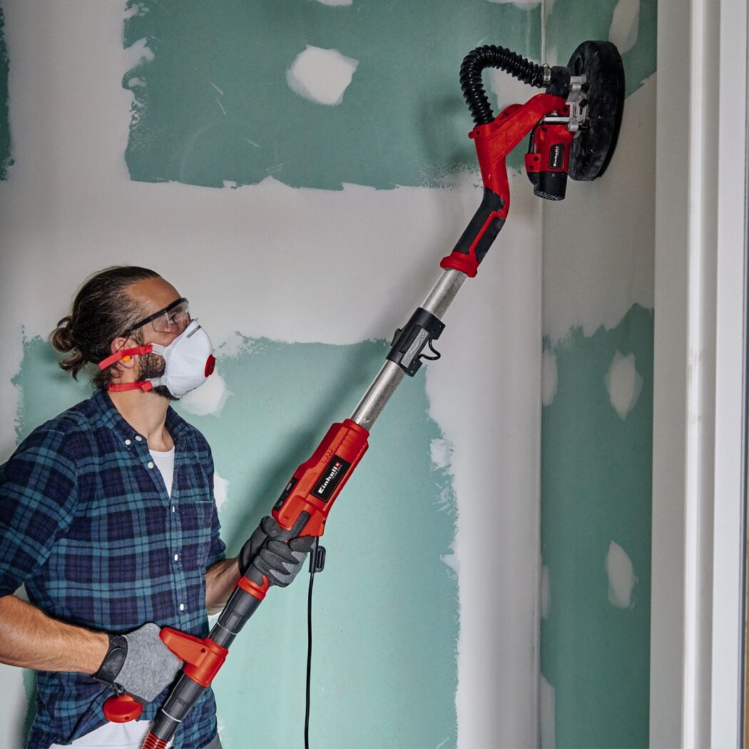 Person schleift mit Trockenbauschleifer eine Wand