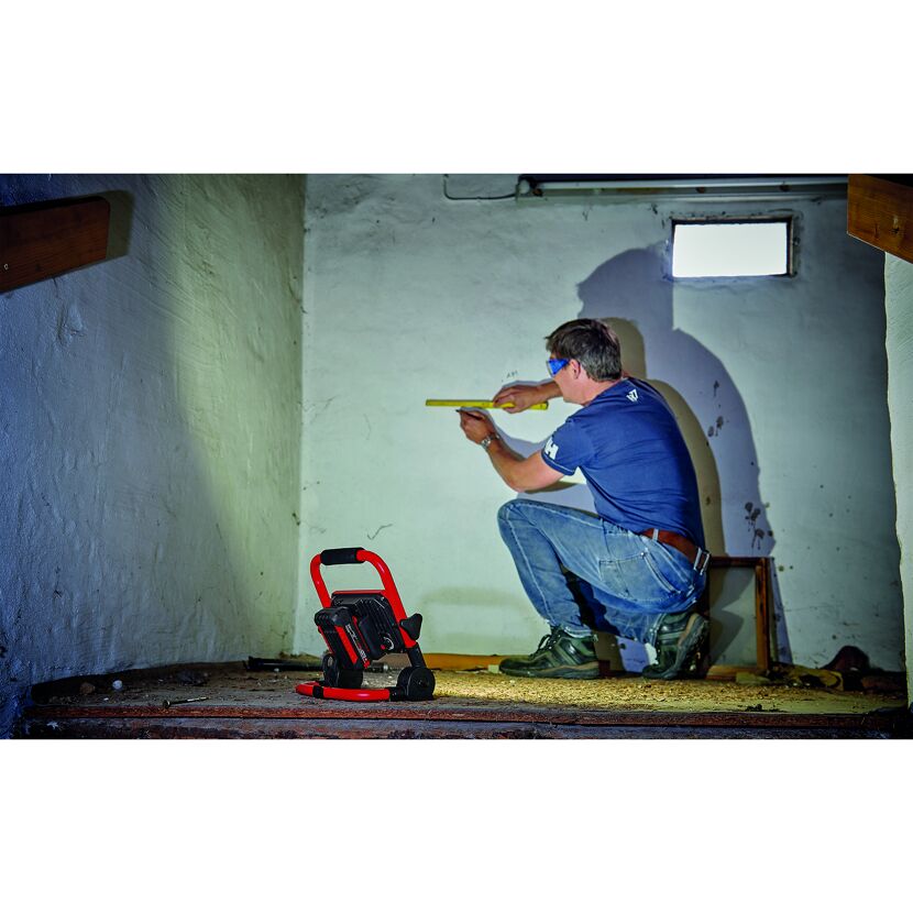 Person misst eine Wand mit Zollstock aus. Beleuchtet wird die Szene mit einer Akku-Lampe.