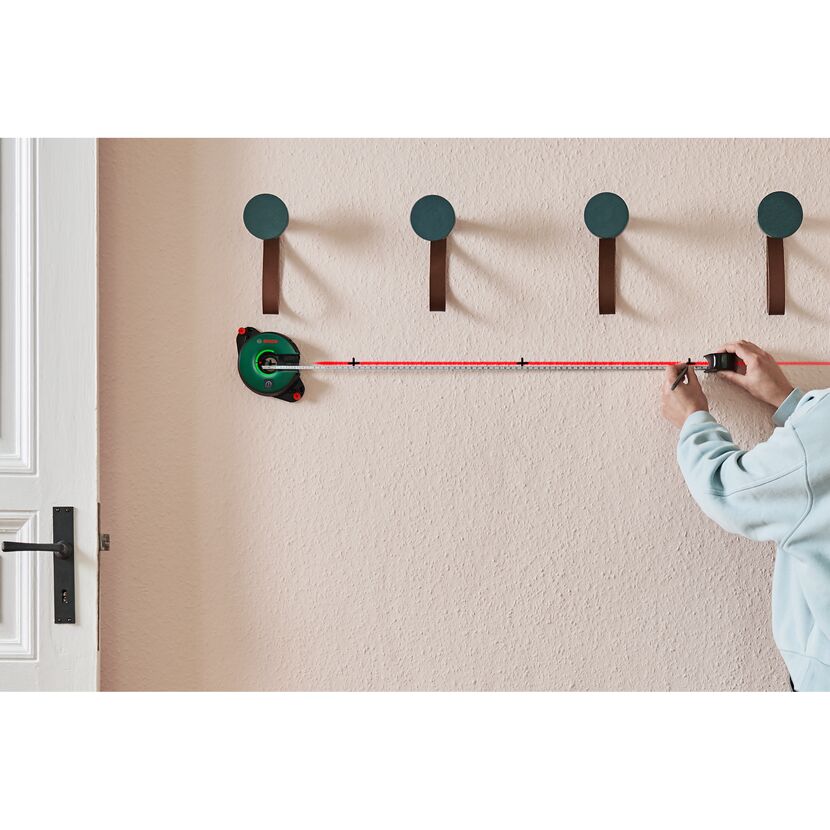 Person markiert eine gerade Linie mit einem Linienlaser an der Wand.