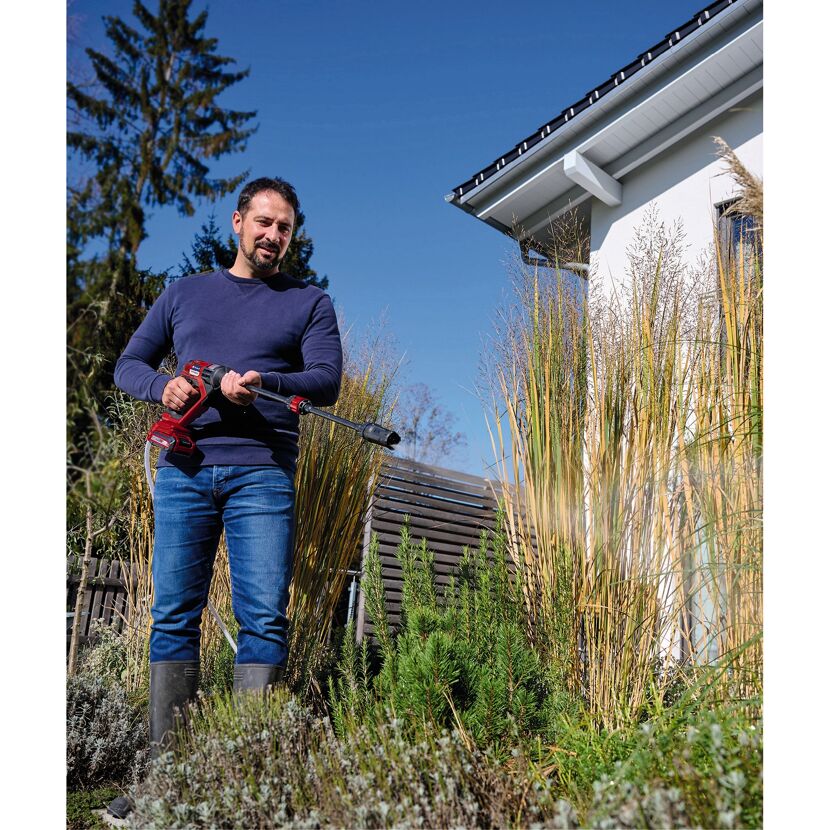 Person verwendet einen Akku-Druckreiniger im Garten.